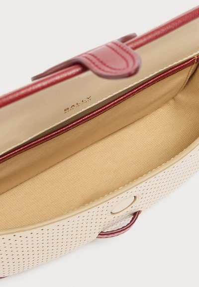 Μπεζ δερμάτινη τσάντα με διάτρητο σχέδιο και κόκκινη επένδυση, ανοιχτή για να αποκαλύψει ευρύχωρο ταμπά εσωτερικό και μαγνητικό κούμπωμα.