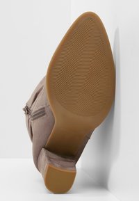 Bottine en daim marron avec une semelle en caoutchouc texturée, dotée d'une fermeture éclair latérale et d'un talon fin, présentant des surfaces lisses et des bords arrondis.