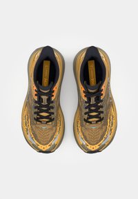 La scarpa presenta un design in camouflage marrone e arancione, una tomaia in rete, lacci neri, colletto imbottito e accenti grigi sulla suola.
