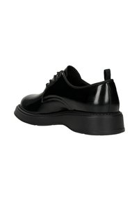 Scarpa in pelle verniciata nera con punta arrotondata, suola piattaforma nera testurizzata e design con lacci, dotata di un piccolo tassello posteriore per facilitare l'inserimento.