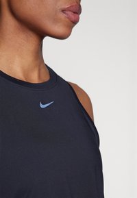 Haut de sport sans manches bleu marine foncé avec un col rond, arborant un logo Nike bleu clair sur la poitrine. Texture de tissu lisse.