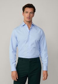 Light blue button-up shirt with long sleeves, featuring a subtle striped pattern, paired with dark green trousers.