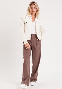Chaqueta de forro polar blanca con dos bolsillos en el pecho, combinada con pantalones de pierna ancha marrones. Zapatillas blancas completan el conjunto. Textura plana y ajuste relajado.