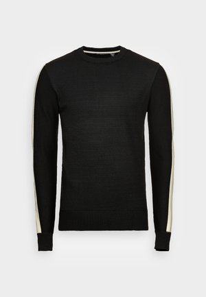 Suéter de punto negro con cuello redondo, que presenta rayas crema a lo largo de los hombros y las mangas. Puños y dobladillo acanalados. Textura suave.