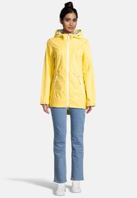 Yellow rain jacket with a zip front, hood, and two side pockets. Features white zippers and a lightweight design. Worn over blue jeans.