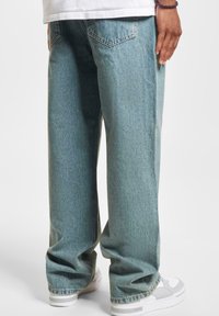Vaqueros de mezclilla de pierna ancha en azul claro con un lavado desvanecido y bolsillos traseros clásicos, combinados con zapatillas blancas con detalles en gris.