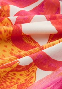 Tissu lisse avec un motif floral audacieux aux couleurs orange, rouge et rose sur fond blanc, plié doucement.