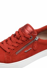 Le sneakers in suede rosso presentano dettagli con zip, lacci testurizzati e una suola in gomma bianca. Logo argentato sul lato e rifiniture in pelle liscia.