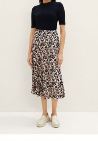Haut côtelé bleu marine à manches courtes associé à une jupe midi plissée à motifs floraux dans des tons de bleu marine, pêche et crème. Porté avec des mocassins de couleur claire.