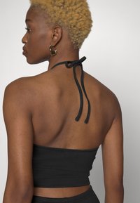 Top cropped preto canelado com alças, apresentando uma textura suave e um design ajustado, combinado com brincos grandes em forma de argola dourada.