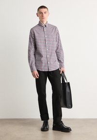 Camicia a quadri rossa, blu e bianca, abbinata a pantaloni neri. Il modello tiene una borsa a tracolla nera e indossa scarpe nere. Tessuto liscio.