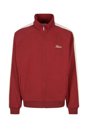 Czerwona kurtka zapinana na zamek błyskawiczny z wysokim kołnierzem, białymi paskami po bokach rękawów, przednimi kieszeniami oraz logo "Kani" na lewej piersi.