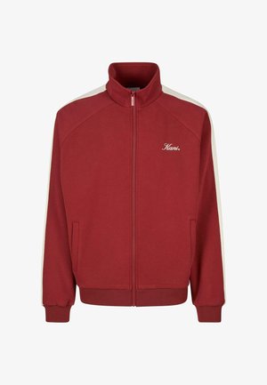 Rød lynlåsjakke med høj krave, hvide sidelister på ærmerne, forreste lommer og "Kani" logo på venstre bryst.