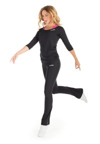 Schwarzes langärmeliges Sportoberteil mit Rundhalsausschnitt, kombiniert mit schwarzen, eng anliegenden Hosen. Beide haben eine glatte Textur und diskrete Logo-Accents.