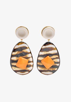 Złote i beżowe okrągłe sztyfty z dużymi wisiorami w kształcie kropli łzy w biało-czarne paski, z każdym ozdobionym pomarańczowym akcentem w kształcie diamentu.