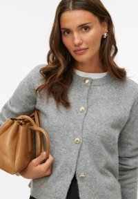 Grå stickad kofta med guldknappar i snäckskalform, rund halsringning och rak passform. Håller en brun läderhandväska med strukturerad form.