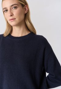 Maglione a costine blu navy con scollo rotondo e spalle scese, caratterizzato da una texture morbida e una vestibilità ampia.