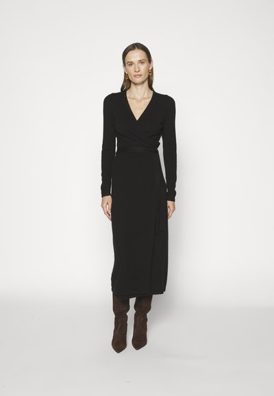 Robe portefeuille noire en matériau doux, dotée de longues manches et d'un décolleté en V profond. Détail de nœud remarquable à la taille et silhouette ajustée.