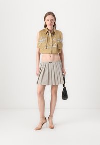 Camicia dorata cropped con motivi bianchi, gonna plissettata a pois neri e bianchi, sandali con tacco nudo e borsa nera.