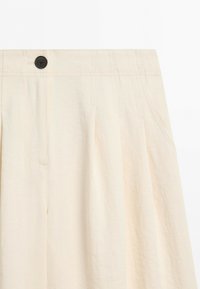 High-waisted cream skirt with pleats, side pockets, waistband stitching, and a single dark button closure at the top front.