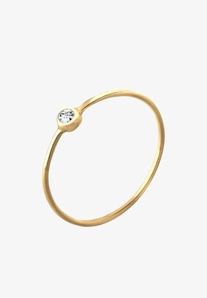 Bague fine en or avec une petite pierre précieuse ronde et claire sertie en chaton sur fond blanc.