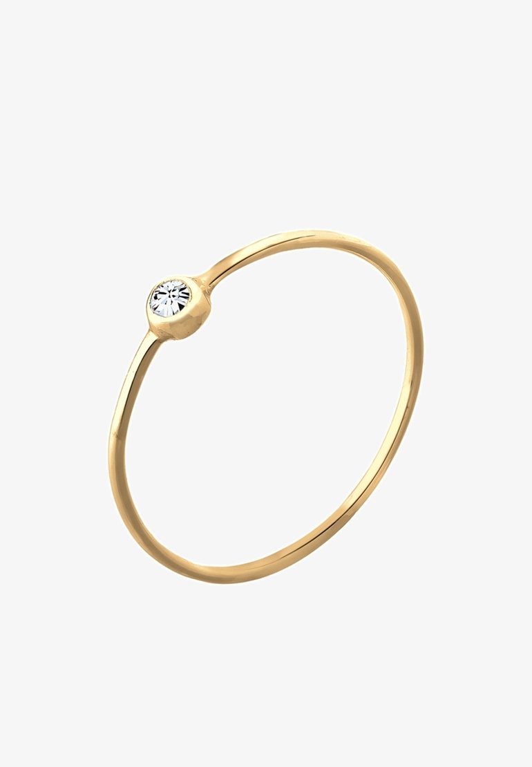 Bague fine en or avec une petite pierre précieuse ronde et claire sertie en chaton sur fond blanc.
