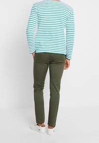 Koszula z długim rękawem w turkusowo-białe paski, dopasowane oliwkowozielone spodnie, noszone z białymi butami wsuwanymi, widziane od tyłu.