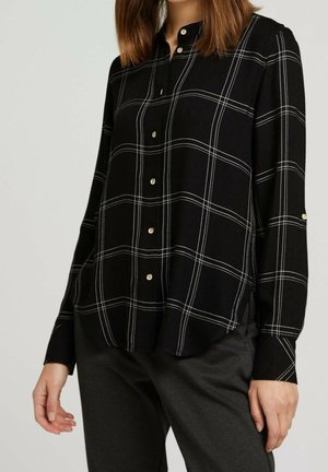 Czarna koszula na guziki z długim rękawem w białą kratę typu windowpane, noszona z ciemnymi spodniami, widok od ramion do bioder.