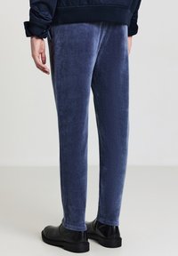 Marineblaue Cordhose aus Cord mit glatter Textur, schmal geschnitten, mit Seitentaschen und getragen zu schwarzen Lederschuhen.