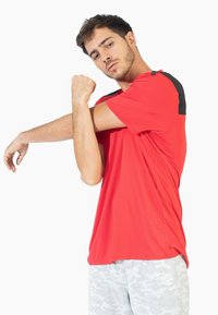 Camiseta atlética roja de manga corta, con acentos negros en los hombros. Textura suave y un corte holgado para mayor comodidad.