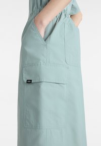 Light teal skirt with an elastic waistband, featuring a large side pocket and Vans logo tag. Made of soft, textured fabric.