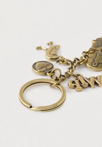 Porte-clés en laiton avec plusieurs breloques, dont un oiseau décoratif et une étiquette ronde, présentant des gravures détaillées et une finition texturée.