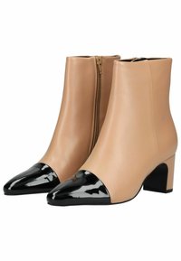 Botines de cuero beige hasta el tobillo con punta en charol negro, cierre de cremallera y un diseño de tacón grueso. Textura suave en toda la superficie.