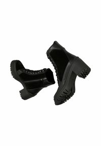 Bottines en cuir noir et daim avec talons épais, lacets à l'avant, fermeture éclair latérale, et semelles à crampons robustes, présentées sur un fond blanc.