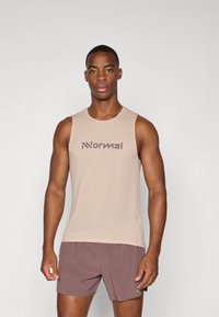 Beige ärmelloses Shirt aus strukturiertem Stoff mit einem dunkelbraunen Logo, kombiniert mit dunkelbraunen Shorts. Einfaches Design, figurbetonte Passform.