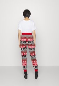 Pantalones de pijama em padrão vermelho e preto com motivos festivos, incluindo flocos de neve e renas, apresentando uma cintura elástica vermelha e punhos canelados.