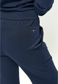 Tumši zili sporta bikses, izgatavotas no mīksta auduma, ar elastīgu jostasvietu un sānu kabatu ar mazu logotipa akcentu.