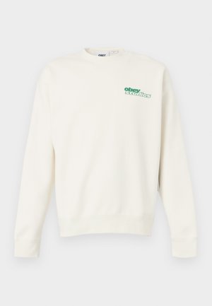 Kremfarget crewneck-genser laget av bomull, med en grønn "obey studios"-logo på brystet. Flate sømmer og ribbestrikkede mansjetter.