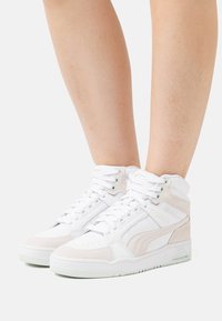 White high-top sneakers made of leather and suede with a textured surface, featuring laces, padded collar, and contrasting accents.