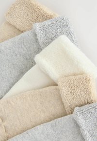 Stak af foldede sokker i beige, grå og hvide nuancer med ribbet og frotté tekstur på en hvid baggrund.