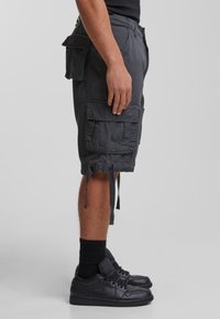 Shorts cargo gris foncé en coton, dotés de plusieurs poches latérales, d'ourlets ajustables avec cordon de serrage et d'une coupe décontractée. Associés à des baskets noires.