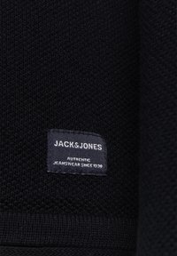 Black textured fabric with a woven pattern featuring a stitched label that reads "JACK & JONES AUTHENTIC JEANSWEAR SINCE 1990."