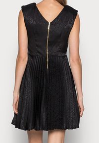 Černé šaty s texturovaným tělem a skládanou sukní. Mají V-výstřih na zádech a zlatý zip. Vyrobené z hladkého, lehkého materiálu.