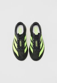 Zwarte sportschoenen met groene accenten, voorzien van drie strepen, een gestructureerde bovenkant en een gewatteerde kraag. De binnenzool toont het woord "ADIZERO."