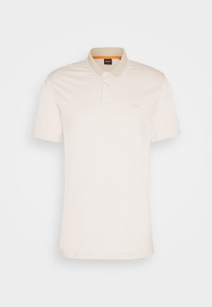 Camisa polo de manga corta en algodón beige claro con un cuello de dos botones, logotipo sutil y acentos de rayas en contraste en el cuello.