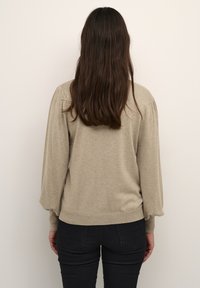 Beige pletený svetr s dlouhými, nafouklými rukávy a žebrovaným lemem, s texturovaným povrchem. V kombinaci s černými úzkými kalhotami.