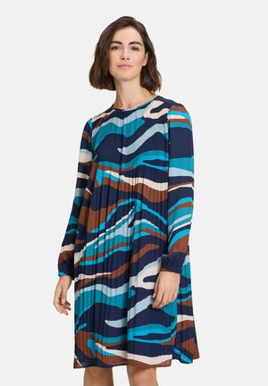 Plissiertes Kleid mit Rundhalsausschnitt, das ein Wellenmuster in Blau, Braun und Creme zeigt. Lange Ärmel mit elastischen Bündchen; leichter Stoff.