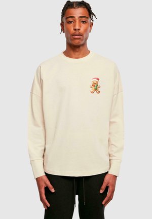 Cremefarvet sweatshirt med lange ærmer, der har et peberkagemand grafik med en rød hat på brystet. Blødt stof og afslappet pasform.