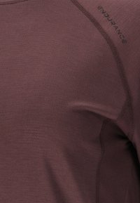 Bordeaux atletisk skjorte lavet af struktureret stof. Har et tætsiddende design og syninger langs skulderen med "ENDURANCE" trykt.