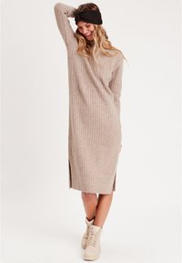 Robe en tricot côtelé beige avec des manches longues, des fentes sur les côtés et un tissu texturé, associée à des bottines crème à lacets et un bandeau noir.